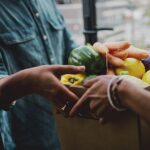 Delivery person handing a box of fresh fruit and vegetables to a customer at the door